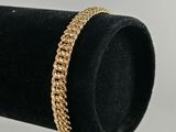 un gros plan d'un bracelet à chaîne en or posé sur un présentoir à bagues noir