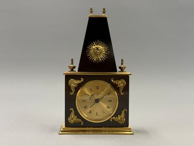l'image d'une petite horloge surmontée d'un soleil