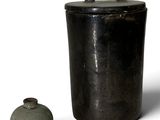 un récipient noir et un vase vert posés sur une surface blanche