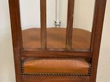 a wooden chair with a leather seat in front of a white wall
