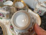 a person holding a tea pot in front of a tray with cups and saucers on it