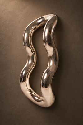sculpture en métal argenté représentant une vague incurvée sur fond marron