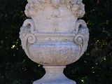 a large stone vase sitting on a pedestal in front of a bush