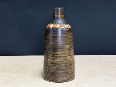 un vase marron posé sur une table, avec un mur noir en arrière-plan