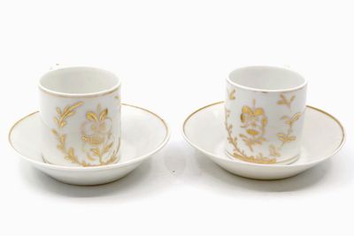 two cups and saucers with gold designs on them on a white surface