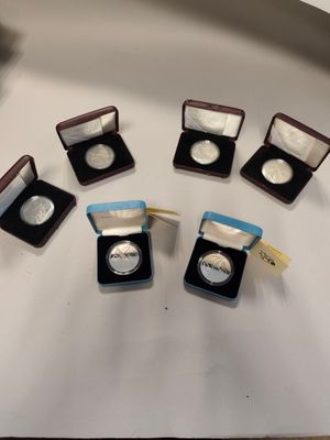 six silver coins are in small cases on a white surface