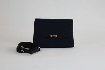 un petit sac à main noir avec un fermoir doré et une ceinture noire