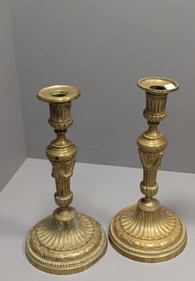 une paire de bougeoirs anciens en laiton posés sur une table blanche