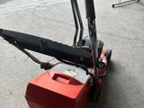 a small red lawn mower sitting on the sidewalk