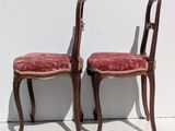 pair of wooden chairs with red upholstered cushions against a white wall