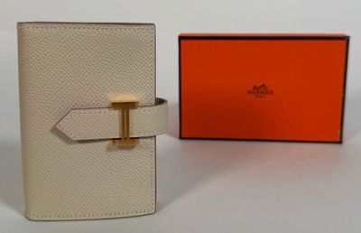 une photo d'un portefeuille blanc orné d'une boucle dorée et d'une boîte orange