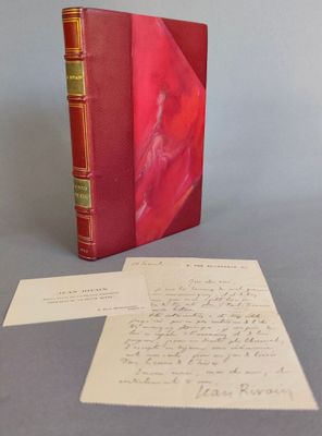 un vieux livre rouge posé sur une table, à côté d'une feuille de papier