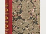 un vieux livre à la couverture rouge posé sur une table blanche