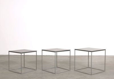 three small tables sitting on top of a cement floor next to a white wall