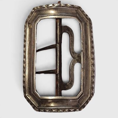 une boucle ancienne en argent sur fond blanc, accompagnée d'une photo en noir et blanc