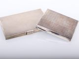 two silver cigarette cases sitting side by side on a white surface