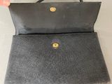 a person holding a black purse with a gold button on it