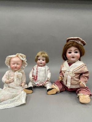 trois poupées en porcelaine assises côte à côte sur une table