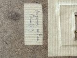 un bout de papier posé par terre, à côté d'un autre bout de papier sur lequel il y a des mots écrits