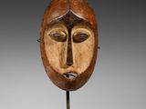 un masque en bois sur un support avec un fond noir
