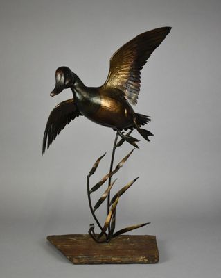 une photo d'une sculpture en bronze représentant un canard posée sur un socle en bois
