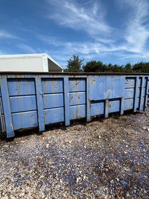 a blue dumpster sitting in the middle of a gravel lot