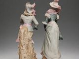 two figurines of women in dresses and hats are standing next to each other