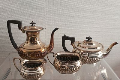trois théières en argent et deux tasses posées sur une table en verre
