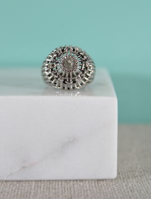 un gros plan d'une bague en argent posée sur un bloc de marbre blanc