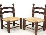 pair of wooden chairs with wicker seats against a white wall