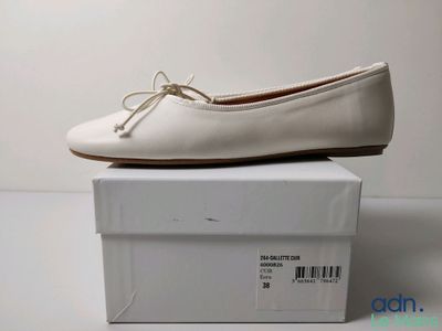 La boîte à chaussures est blanche et il y a une paire de chaussures posée dessus.