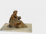 une statue représentant une femme en train de lire un livre, posée sur un socle en marbre