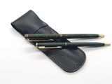 two green pens and a black case on a white surface