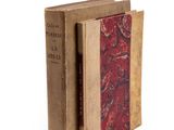 an old book with a red cover sitting on top of a white surface