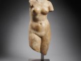 une statue en marbre représentant un torse féminin, posée sur un socle