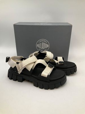 une paire de sandales noires et blanches avec une boîte en arrière-plan