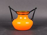 an orange vase with a black handle on a table