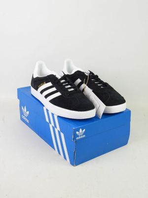 des baskets adidas noires et blanches posées sur une boîte bleue, sur fond blanc