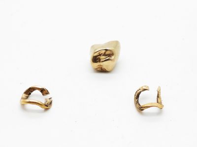 trois paires de boucles d'oreilles en or et une bague en or posées sur un fond blanc