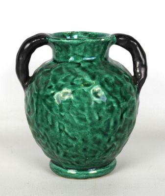 un vase vert muni d'une anse noire sur un fond blanc