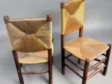 two wooden chairs with woven seats on a gray surface
