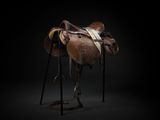an old saddle on a stand against a black background