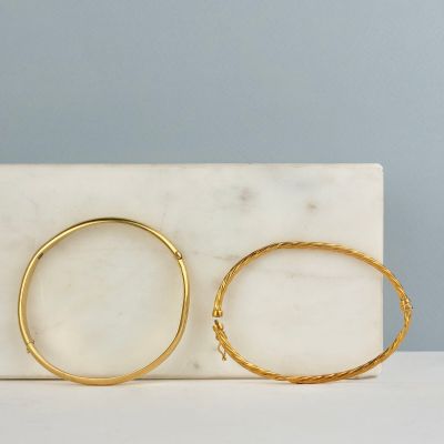une paire de boucles d'oreilles créoles en or posée sur un bloc de marbre