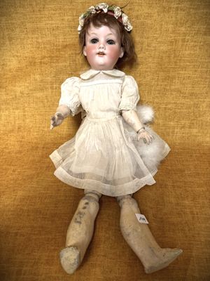 une poupée à l'ancienne, vêtue d'une robe blanche et portant un serre-tête orné d'une fleur