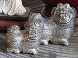 two silver figurines sitting on a table next to a red vase