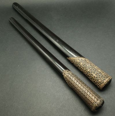 two black and gold handled chopsticks sitting on a black surface