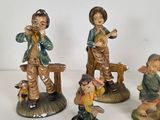 four figurines of children playing music and singing on a white surface