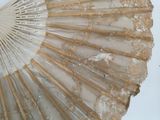 a white fan with gold lace on it sitting on a table