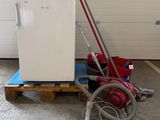 un réfrigérateur blanc et un aspirateur rouge posés sur une palette dans un garage