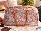 a floral bag sitting on a bed next to a hat and sunglasses